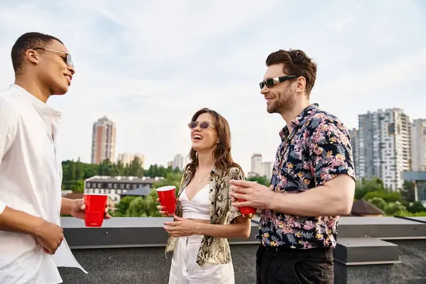 Веселі багаторасові друзі зі стильними сонцезахисними окулярами, що п'ють з червоних чашок під час вечірки на даху — стокове фото