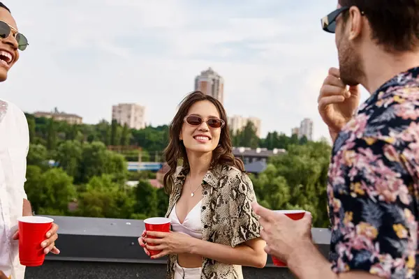 Joyous interracial friends in casual attire with sunglasses drinking from red cups on rooftop — Stock Photo