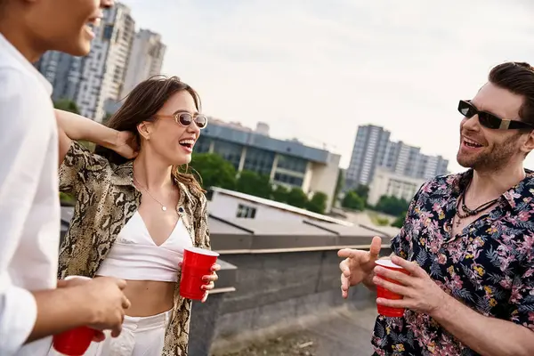 Fröhliche Freunde in pulsierendem Outfit trinken bei gemeinsamer Dachparty aus roten Tassen — Stockfoto