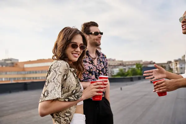 Joyous woman looking at camera surrounded by her interracial jolly male friends at rooftop party — Stock Photo