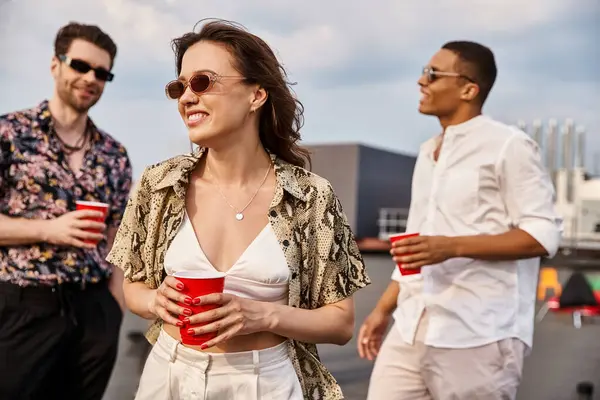 Joyous woman in vibrant attire surrounded by her diverse jolly male friends at rooftop party — Stock Photo