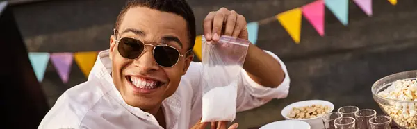 Jolly african american man with sunglasses holding bag of salt and smiling at camera, banner — Stock Photo