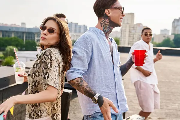 Amis multiraciaux joyeux avec des lunettes de soleil boire des cocktails à la fête sur le toit et danser au DJ set — Photo de stock
