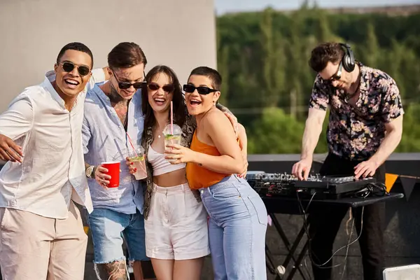 Cheerful interracial friends with drinks posing next to DJ at rooftop party and smiling at camera — Stock Photo