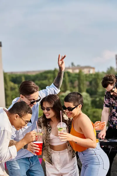 Amigos multirraciais alegres com óculos de sol elegantes bebendo coquetéis ao lado de DJ na festa no telhado — Fotografia de Stock