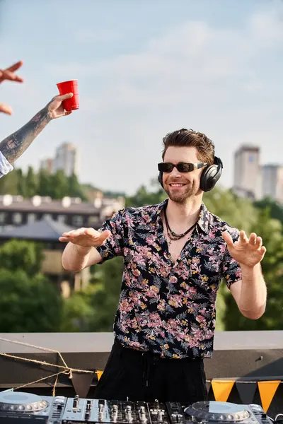 Apuesto DJ alegre con gafas de sol con estilo en traje vibrante tocando música en la fiesta en la azotea - foto de stock