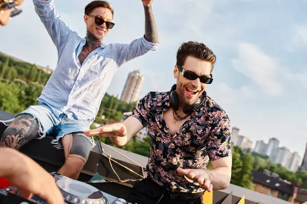 Alegre gente guapa en vibrantes trajes urbanos con gafas de sol de fiesta en la azotea para DJ conjunto - foto de stock