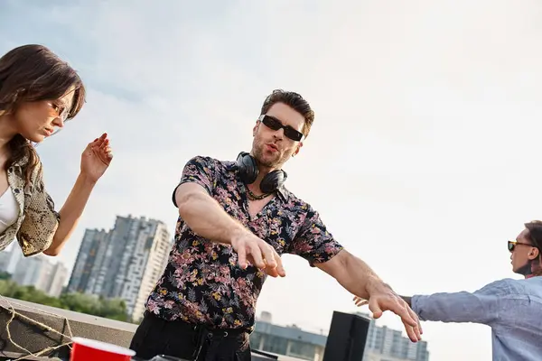 Молодые привлекательные веселые люди в стильных одеждах с коктейлями, танцующими с DJ на вечеринке на крыше — стоковое фото
