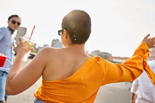 Fashionable young woman with alcohol drink in hand partying on rooftop with her tattooed friend — Stock Photo