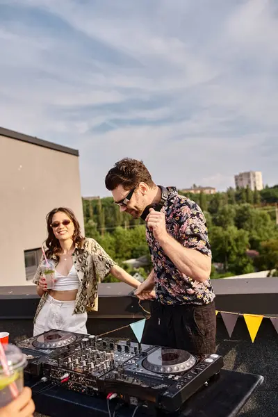 Joyeuse jeune femme avec des lunettes de soleil tenant cocktail et relaxant à côté de DJ à la fête sur le toit — Photo de stock