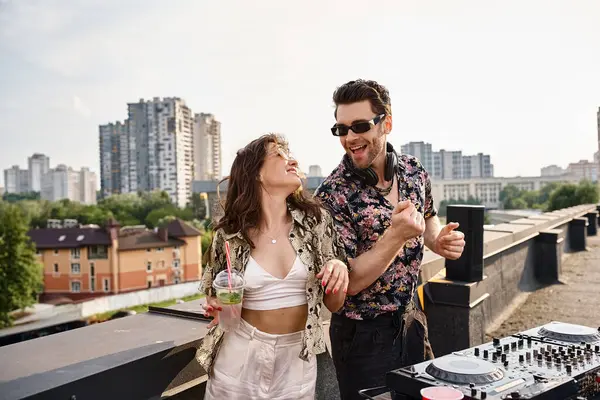 Jolly beautiful woman with cocktail dancing with handsome joyous DJ to music at rooftop party — Stock Photo