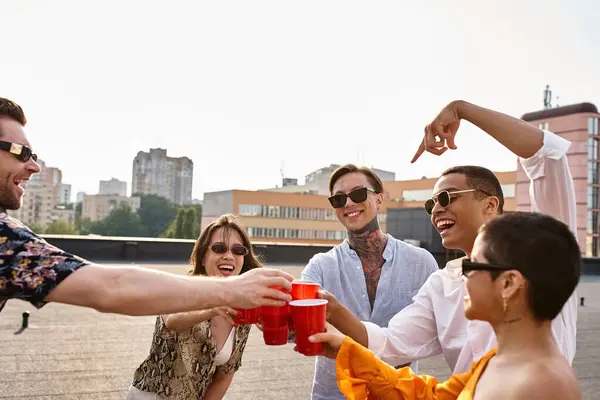 Atractivo alegre interracial amigos tintineo su rojo tazas al lado de DJ equipo en la fiesta - foto de stock