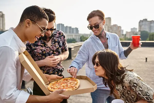 Amigos inter-raciais alegres com óculos de sol elegantes compartilhando pizza e se divertindo na festa no telhado — Fotografia de Stock