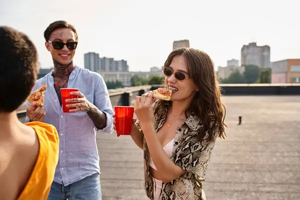 Amigos alegres de buen aspecto en atuendos vívidos casuales comer pizza y disfrutar de bebidas en la fiesta - foto de stock