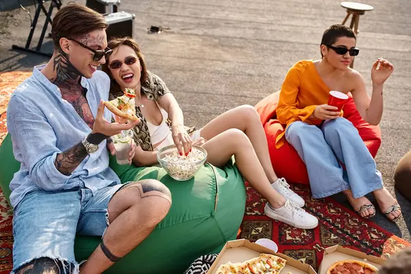 Amigos alegres de buen aspecto en trajes elegantes disfrutando de pizza y bebidas en la fiesta en la azotea - foto de stock