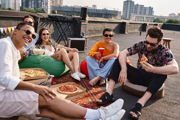 Amigos multiculturales alegres en trajes vibrantes con gafas de sol disfrutando de pizza y bebidas en la fiesta - foto de stock