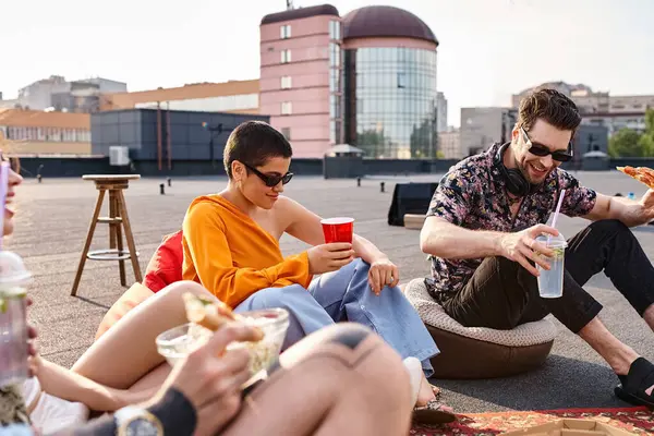 Attractive jolly friends in urban attires sitting on rooftop eating pizza and drinking cocktails — Stock Photo