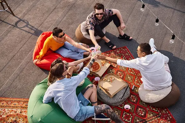 Vista superior de cinco amigos alegres diversos disfrutando de la pizza y tazas de tintineo con bebidas en la fiesta en la azotea - foto de stock