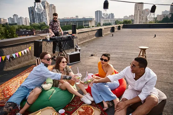 Multicultural attractive friends in stylish outfits clinking their cups with cocktails at rooftop — Stock Photo