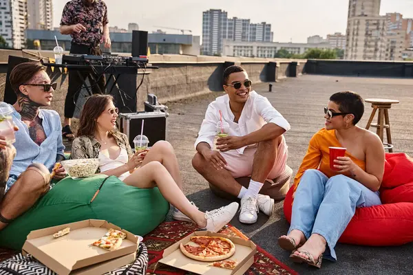 Jolly diverse friends in casual attires enjoying cocktails at rooftop party with DJ on backdrop — Stock Photo