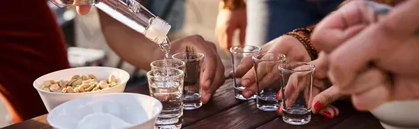 Cropped view of interracial young friends pouring tequila shots while at rooftop party, banner — Stock Photo