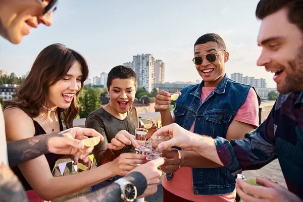 Group of cheerful multicultural friends drinking tequila with fresh lime and salt at rooftop party — Stock Photo