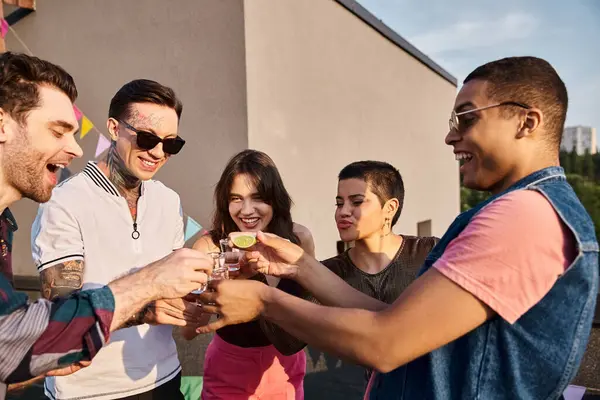 Весьма разнообразные друзья в стильных солнечных очках пьют текилу с лаймом и солью на вечеринке на крыше — стоковое фото