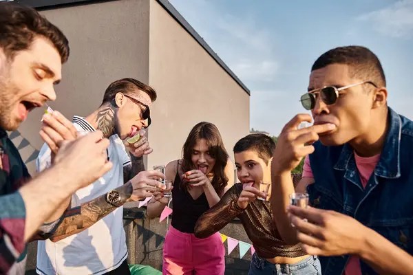Alegre diversos amigos con gafas de sol de moda beber tequila con lima y sal en la fiesta en la azotea - foto de stock