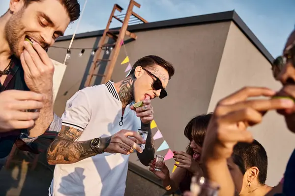 Joyful interracial friends with stylish sunglasses drinking tequila with lime and salt at party — Stock Photo