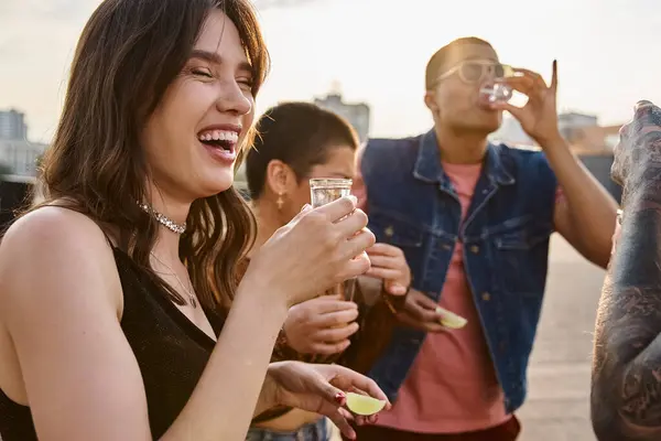 Joyful multicultural people in vibrant clothing enjoying tequila with salt and lime at rooftop party — Stock Photo