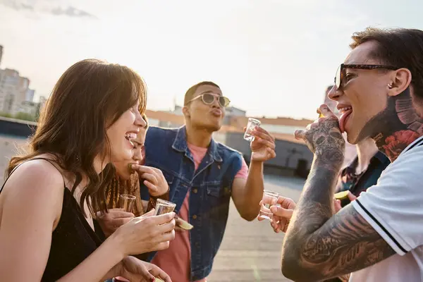 Fröhliche gemischtrassige Menschen in lebendiger Kleidung genießen Tequila mit Salz und Limette auf einer Dachparty — Stockfoto