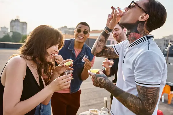 Jolly multicultural people in vibrant clothes enjoying tequila with salt and lime at rooftop party — Stock Photo