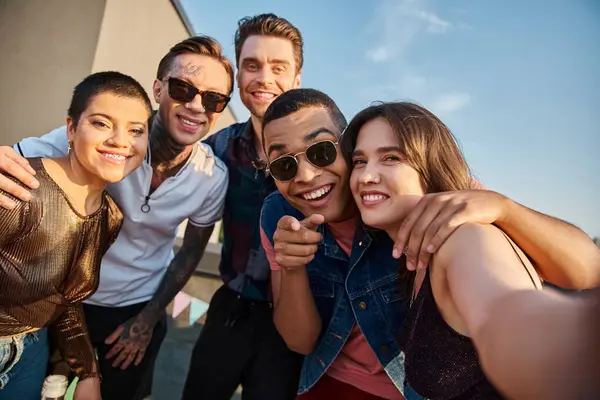 Attractive jolly multiracial friends posing together on rooftop and smiling happily at camera — Stock Photo