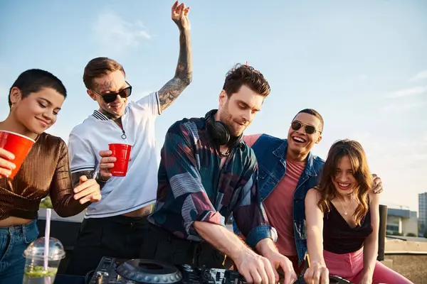 Pessoas alegres multiculturais em roupas vívidas festejando juntos ao lado de DJ atraente na festa no telhado — Fotografia de Stock