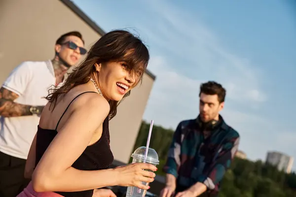 Fokus auf fröhliche attraktive Frau, die neben ihren verschwommenen Freunden auf einer Dachparty in die Kamera blickt — Stockfoto