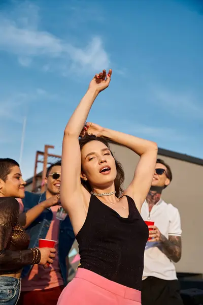 Focus on merry pretty woman looking at camera near her blurred diverse friends at rooftop party — Stock Photo