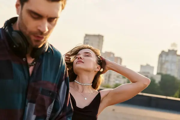 Gut aussehende langhaarige Frau in urbaner Kleidung, die neben einem gutaussehenden DJ auf einer Dachparty chillt — Stockfoto