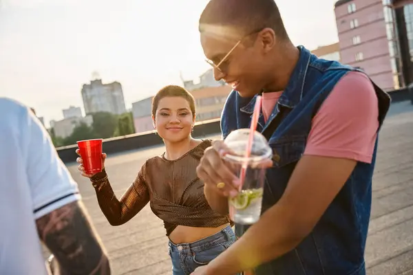 Cheerful short haired woman in urban attire smiling at camera next to her diverse friends at party — Stock Photo