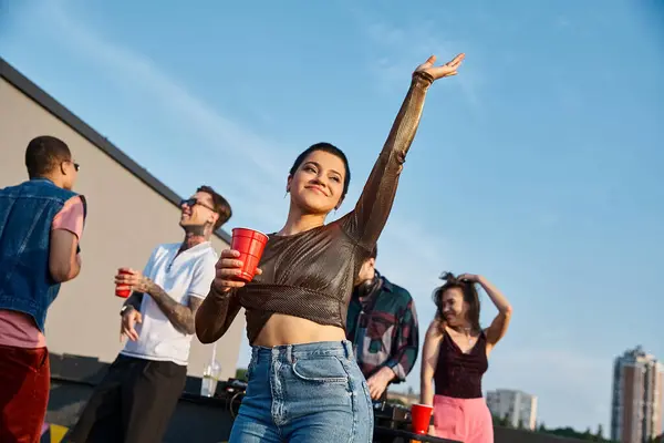 Lustige attraktive Frau in lebendigem Outfit mit Cocktail und Spaß neben ihren vielfältigen Freunden — Stockfoto