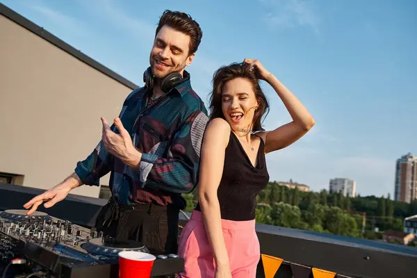 Joyeuse femme attrayante avec les cheveux longs s'amuser à la fête sur le toit à côté de beau DJ joyeux — Photo de stock
