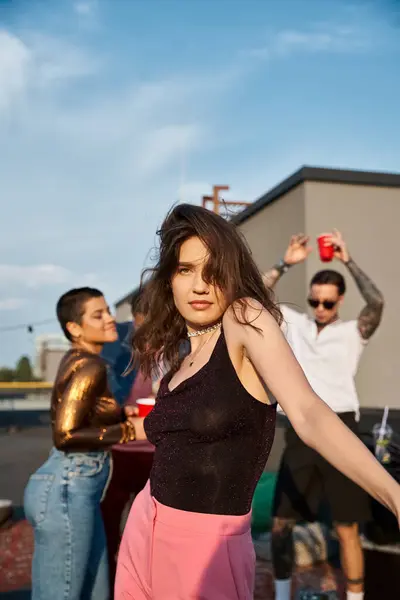 Focus on jolly appealing woman in vivid attire partying next to her jolly blurred friends on rooftop — Stock Photo