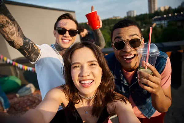 Весёлые мультикультурные друзья держат коктейли в руках и веселятся на вечеринке на крыше — стоковое фото