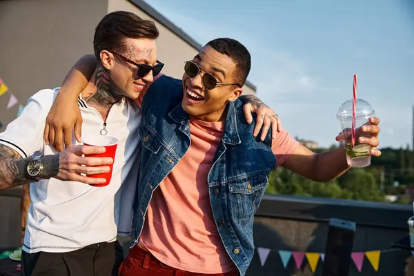 Good looking cheerful diverse men holding cocktails and looking at each other at rooftop party — Stock Photo