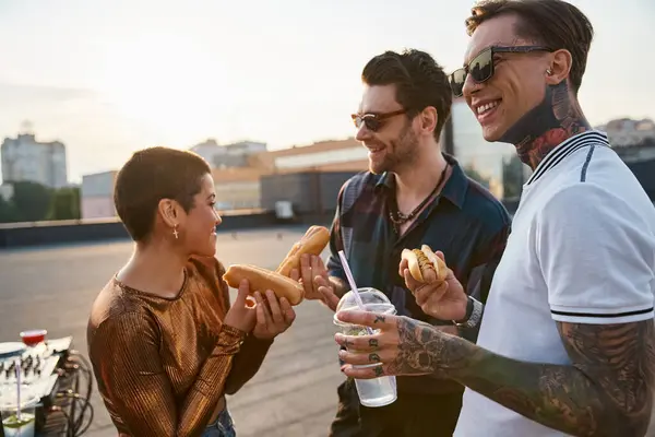 Joyous good looking friends with sunglasses in urban outfits enjoying hot dogs at rooftop party — Stock Photo