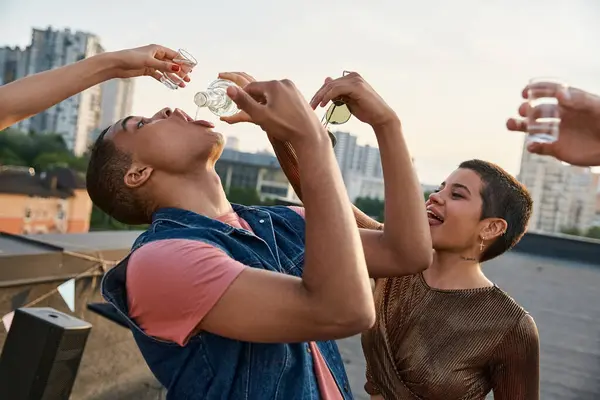 Fröhliche junge Leute in stylischen Outfits gießen ihrem afrikanisch-amerikanischen Freund Tequila in den Mund — Stockfoto