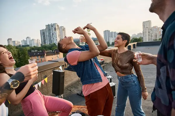 Jolly attractive people in stylish outfits pouring tequila in mouth of their african american friend — Stock Photo