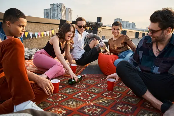 Attractive cheerful multicultural friends playing spin the bottle together at rooftop party — Stock Photo