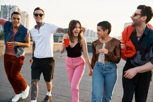 Cheerful diverse friends walking with different drinks and bean bag chair in hands at rooftop party — Stock Photo