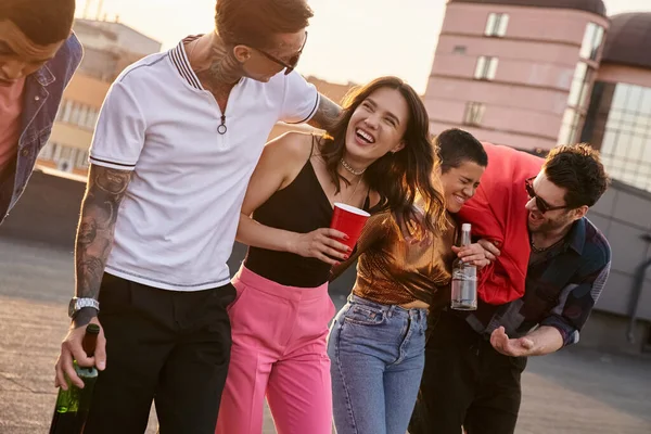 Drunk cheerful multicultural friends in urban outfits holding alcohol drinks and having fun at party — Stock Photo