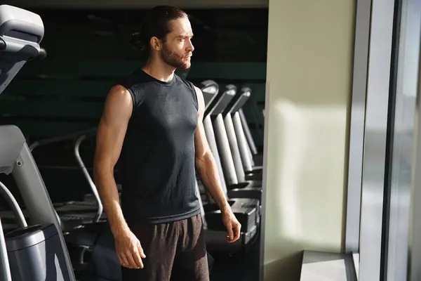 A man in active wear stands confidently in front of a row of treadmills in a gym, ready for a vigorous workout. — Stock Photo